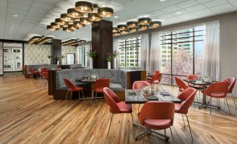 a modern restaurant with wooden floors , red chairs , and a bar area , under a high ceiling with large windows at Hyatt Centric Arlington