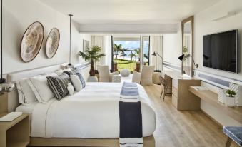 a luxurious hotel room with a large bed , white bedding , and a view of the ocean through a window at Lux* Grand Gaube