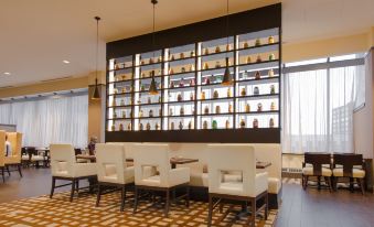 a modern dining room with a long dining table surrounded by chairs , and a bookshelf filled with various bottles on the wall at Hilton Albany