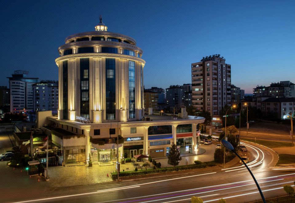 a large building with a tower on the corner of a street at night , surrounded by tall buildings and cars at DoubleTree by Hilton Gaziantep