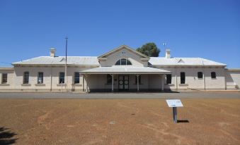 a large white building with a sign in front of it , surrounded by a dirt lot at Coolgardie GoldRush Motels