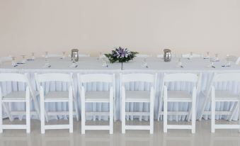 a long dining table set for a formal event , with white chairs arranged around it at Travellers Beach Resort