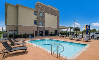 a large swimming pool with a stone exterior and lounge chairs is located in front of a building at Comfort Inn & Suites Victoria North