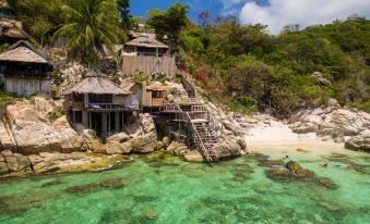 a beach house situated on a rocky coastline , with clear blue water and a sandy beach at Taatoh Seaview Resort