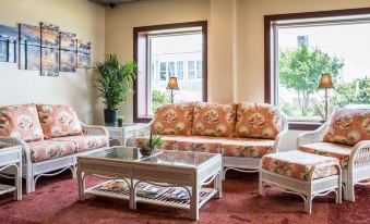 a living room with a large window , floral couches , and coffee table , set against the backdrop of a red carpet and white walls at Island Inn & Suites, Ascend Hotel Collection