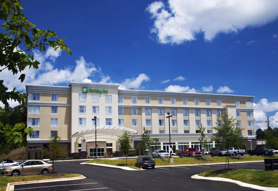 a holiday inn hotel with its parking lot , trees , and cars in the foreground , under a clear blue sky at Holiday Inn Birmingham - Hoover
