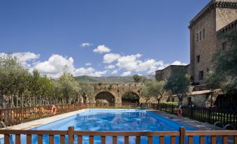 a large swimming pool surrounded by a wooden fence , with a stone bridge in the background at Parador de Jarandilla