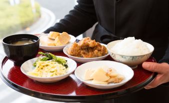 a woman is holding a tray filled with various dishes , including fried chicken , rice , and vegetables at Kochi Hotel