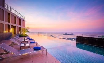 a rooftop pool overlooking the ocean , with lounge chairs and umbrellas placed around it for relaxation at Somerset Harbourview Sri Racha
