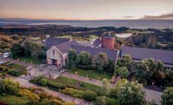 aerial view of a large building surrounded by greenery and trees , with a body of water in the background at Rosewood Cape Kidnappers