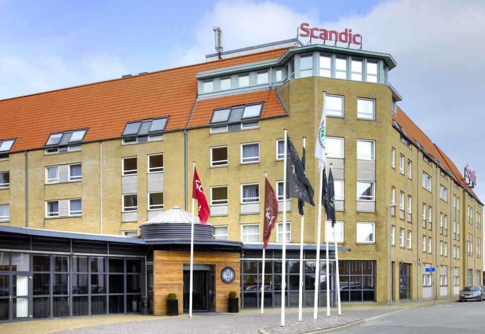 "a large brick building with a red sign that says "" scandic "" and several flags on the outside" at Scandic the Reef