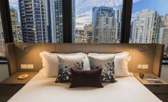 a bed with white sheets and pillows is situated in front of a window that overlooks a city skyline at Capri by Fraser Brisbane
