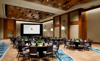 a large conference room with tables and chairs , a screen displaying the hilton logo , and wooden ceiling at Raleigh Marriott Crabtree Valley