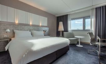 a large bed with white linens is in a room with a window , lamp , and chair at Radisson Blu Airport Hotel, Oslo Gardermoen