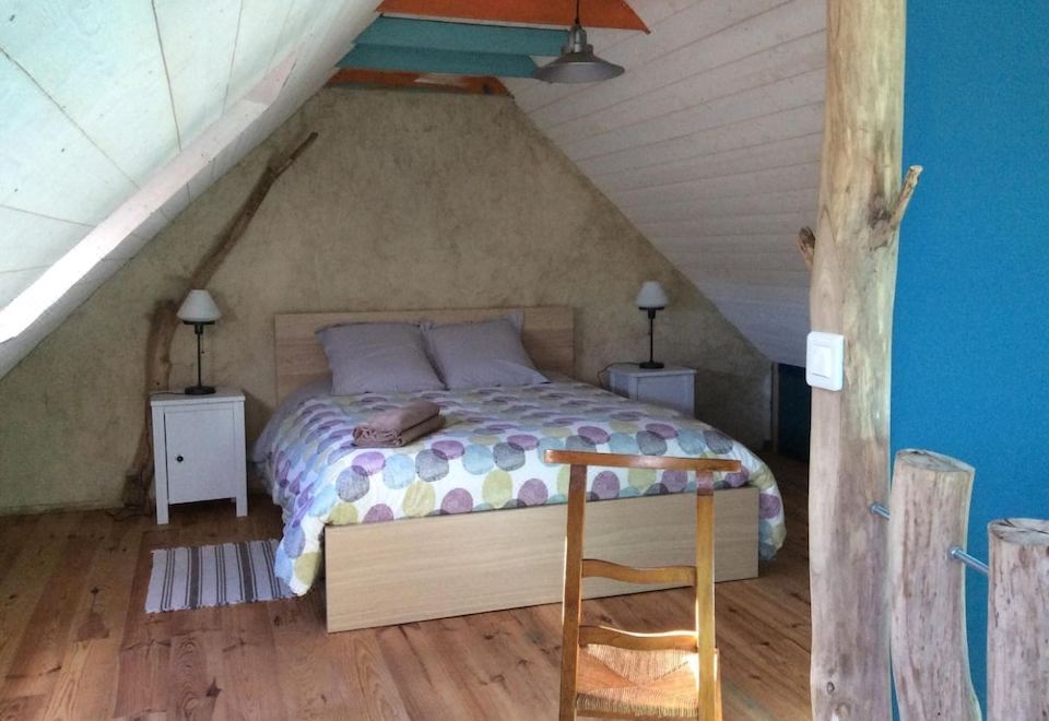 a cozy attic bedroom with wooden floors , white walls , and a large bed decorated with colorful pillows at La Vieille Ferme