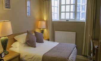 a neatly made bed with white sheets and pillows is situated in a room next to a window at The Kings Head Hotel