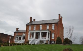 a large brick house surrounded by a grassy field , with a fence surrounding the property at General Morgan Inn