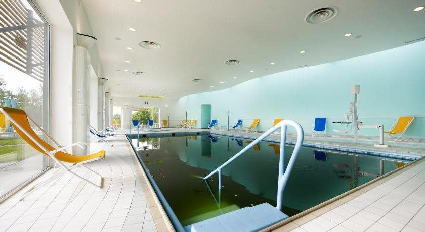 an indoor swimming pool surrounded by white walls , with lounge chairs and umbrellas placed around the pool at Ana Hotels Europa Eforie Nord