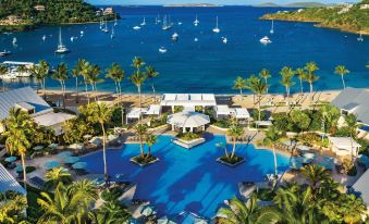 a large outdoor swimming pool surrounded by palm trees and a body of water , with boats in the distance at The Westin St. John Resort Villas