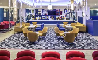 a modern lounge area with yellow and blue chairs , red seating , and a black and white checkered floor at Mercure Swansea Hotel