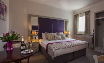 a large bed with a purple headboard is in a hotel room next to a window and a table with champagne at Breffni Arms Hotel