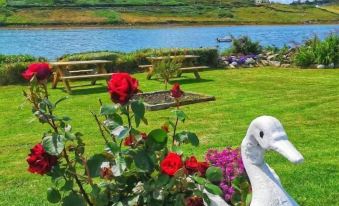 a large white duck statue is sitting next to a flower pot in a grassy field , surrounded by trees and a lake in the background at Ocean Villa