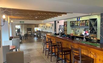 a well - lit bar area with a long wooden bar and several stools surrounding it , creating a lively atmosphere at The Village Inn