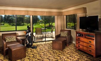 a well - furnished living room with a couch , chairs , and television in front of a large window overlooking a golf course at Sycuan Golf Resort