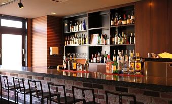 a well - stocked bar with numerous bottles and glasses , as well as a dining table in the background at Hotel Wing International Chitose