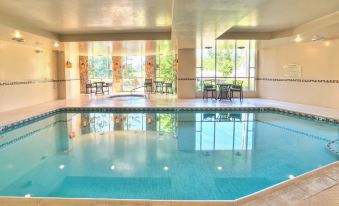 an indoor swimming pool with a large window , surrounded by tables and chairs , in a well - lit room at Hilton Garden Inn Boise/Eagle