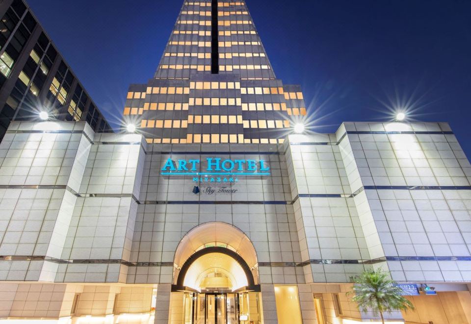a tall hotel building with a large sign above the entrance , illuminated at night at Art Hotel Miyazaki Sky Tower