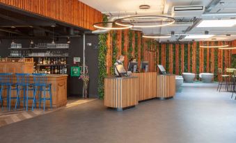 a modern reception area with wooden walls , green vines , and a woman sitting behind a desk at Best Western Plus Hotel Amstelveen