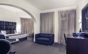 a hotel room with a blue couch , white bed , and gray curtains , along with other furniture at Mercure Maitland Monte Pio