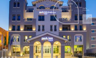 the exterior of a modern building named park inn by radisson hotel , with its name written in large letters and illuminated by the setting sun at Park Inn by Radisson Dammam
