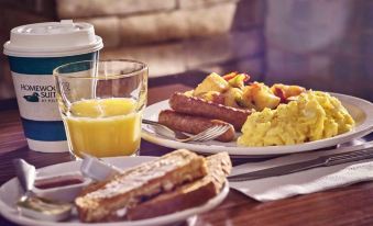 a dining table with a variety of food items , including breakfast plates , toast , eggs , and a glass of orange juice at Homewood Suites by Hilton Rochester - Victor