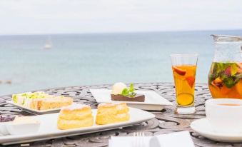 a table with plates of food and a glass of tea , overlooking the ocean on a patio at The Bay Hotel