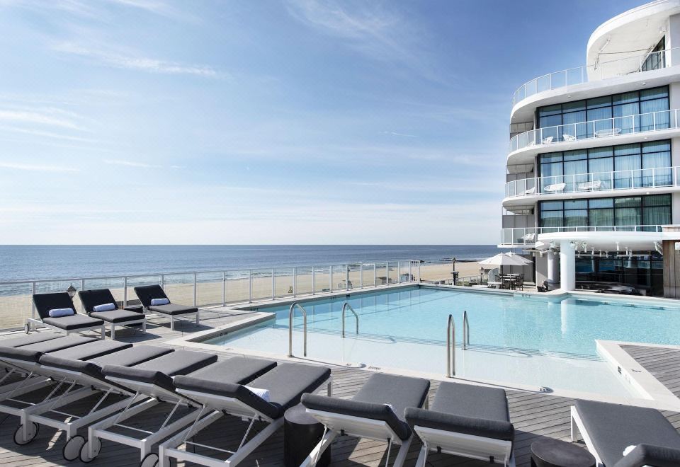 a large swimming pool with lounge chairs and umbrellas , overlooking the ocean and a beach at Wave Resort