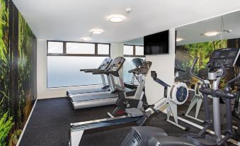 a gym with various exercise equipment , including treadmills and stationary bikes , is situated near a window at Novotel Queenstown Lakeside