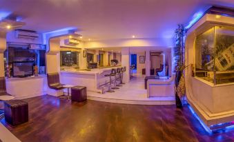 a modern lounge area with wooden flooring , white furniture , and blue lights , as well as a bar area with stools and a television at The Presidency