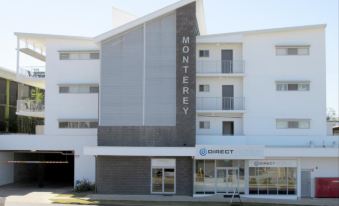 "a modern , white building with gray accents and a large "" monterey "" sign on the front" at Monterey Apartments Moranbah