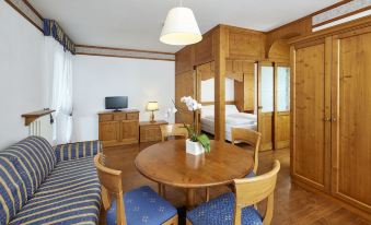 a dining room with a wooden dining table and chairs , a couch , and a television at Grand Hotel Misurina