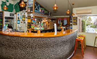 a bar with a curved wooden counter and stools , surrounded by shelves filled with bottles and decorations at The Lodge