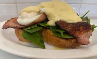 a white plate with a sandwich on it , topped with eggs benedict , bacon , and greens at Parry Creek Farm Tourist Resort & Caravan Park