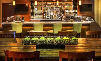 a well - lit bar with a long wooden table and several chairs , as well as a television in the background at DoubleTree by Hilton Portland - Tigard