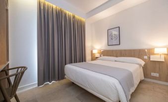 a neatly made bed with white sheets is situated in a bedroom next to a window at Hotel Victori