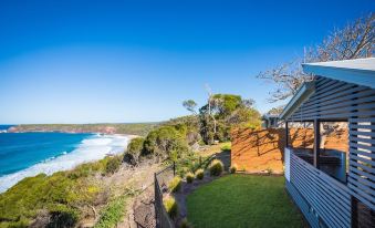 a house with a beautiful view of the ocean and trees , situated on a hillside overlooking the ocean at NRMA Merimbula Beach Holiday Resort