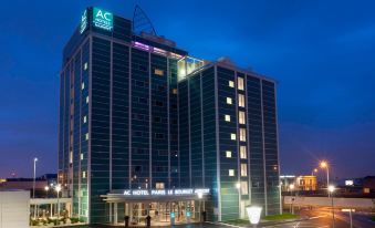 the ac hotel by marriott hotel is shown at night with its lit - up sign and surrounding surrounding area at AC Hotel Paris le Bourget Airport