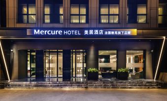 The entrance to a hotel is illuminated at night with a sign above it, surrounded by other buildings at Mercure Shanghai Yu Garden On the Bund