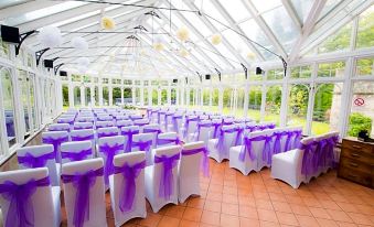 a large , white wedding venue with purple ribbons draped over chairs and umbrellas , set up for a formal event at Kincaid House Hotel