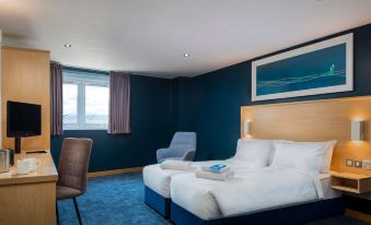 a hotel room with two beds , a desk , and a window , decorated in blue walls and carpet at Travelodge London Chessington Tolworth